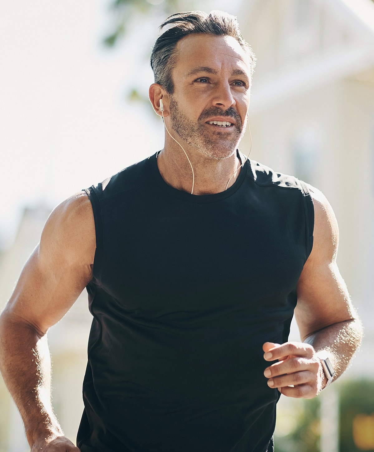 Man jogging with earbuds in sunny environment.