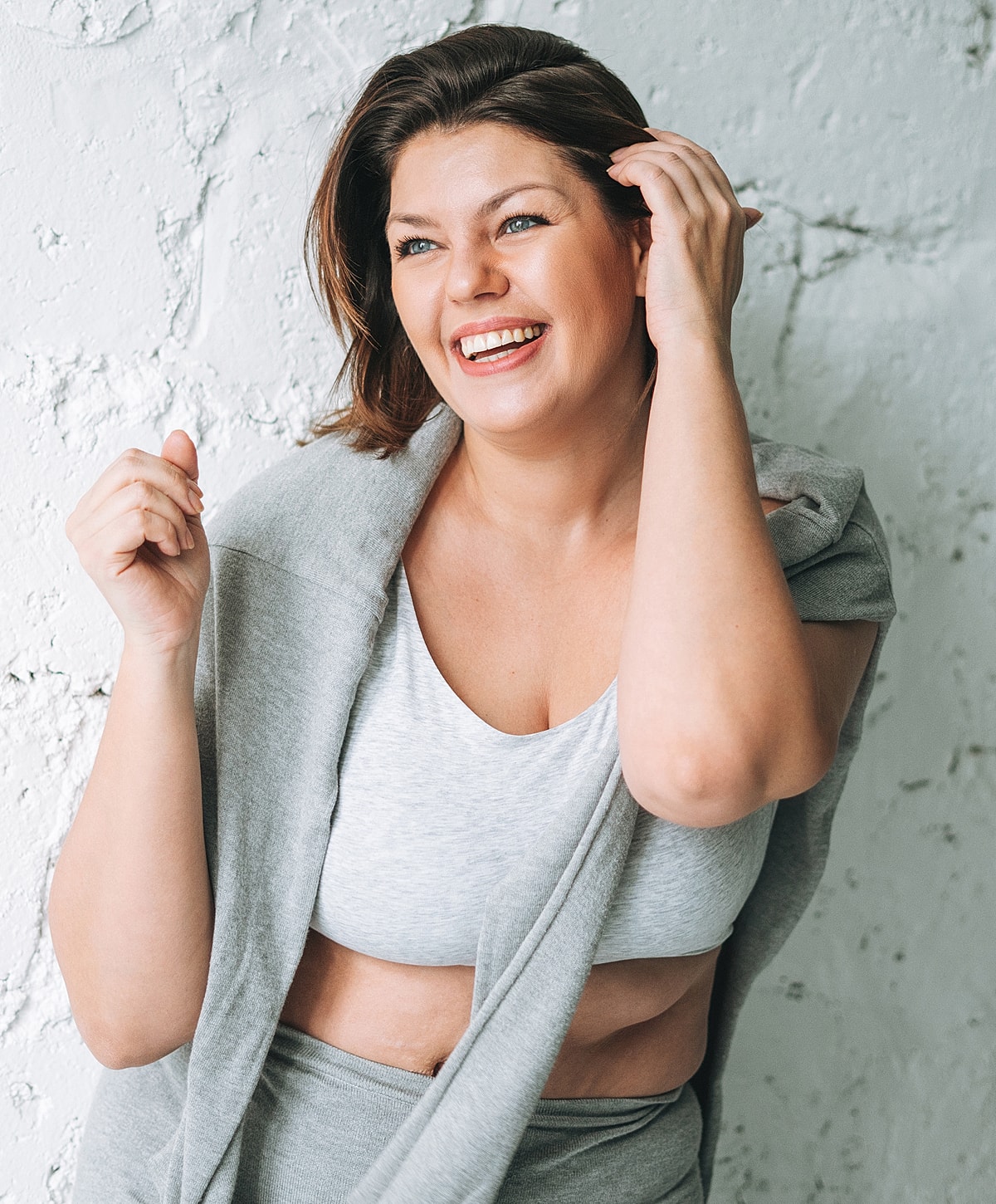Smiling woman in casual gray outfit against wall.